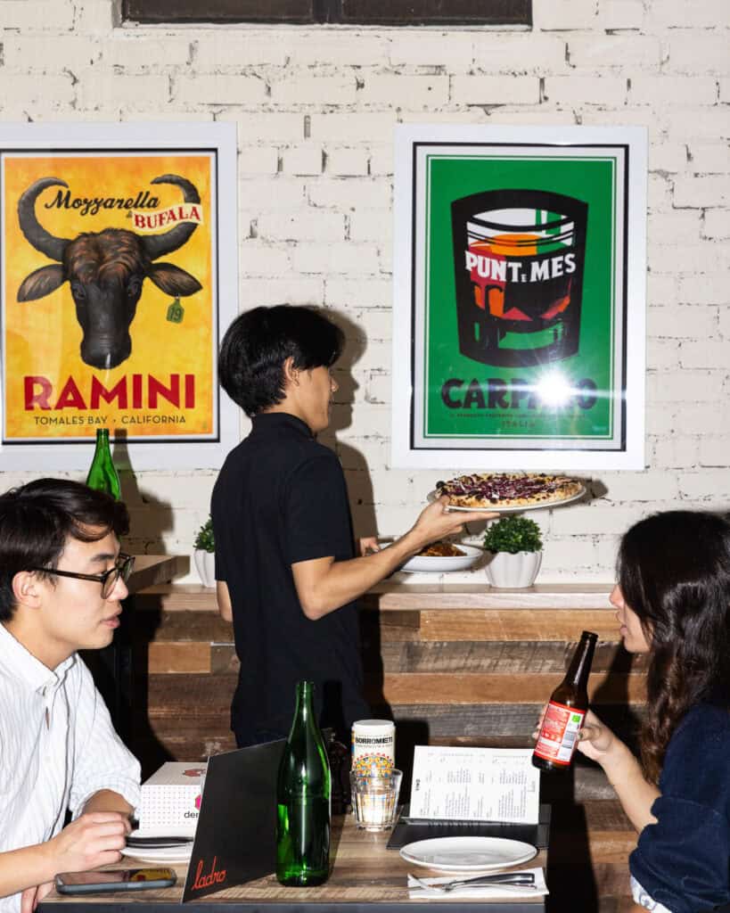 Restaurant scene with people, pizza, and vintage posters.