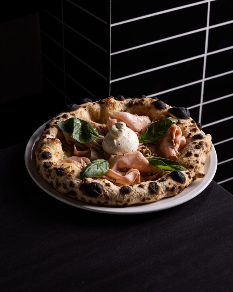 Gourmet pizza with prosciutto, basil, and burrata cheese.