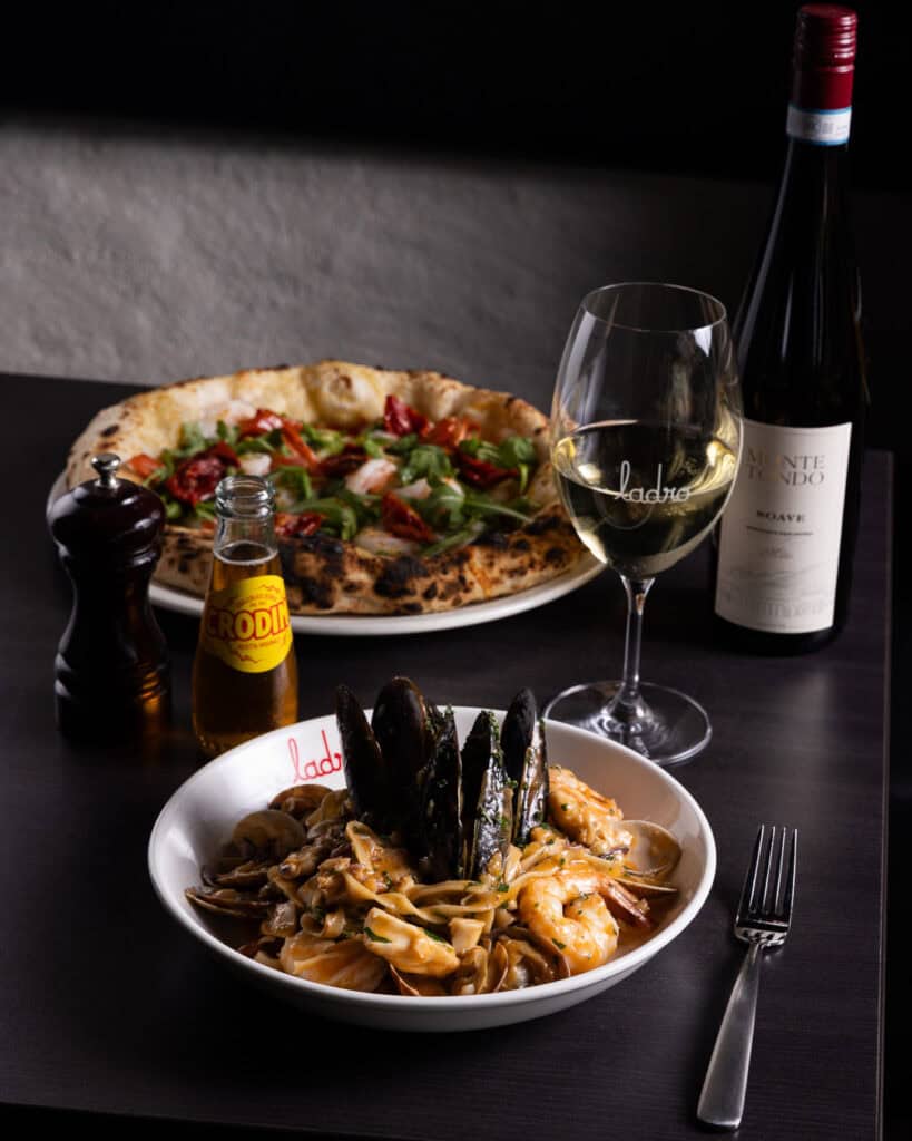 Seafood pasta, pizza, wine, and soda on table.